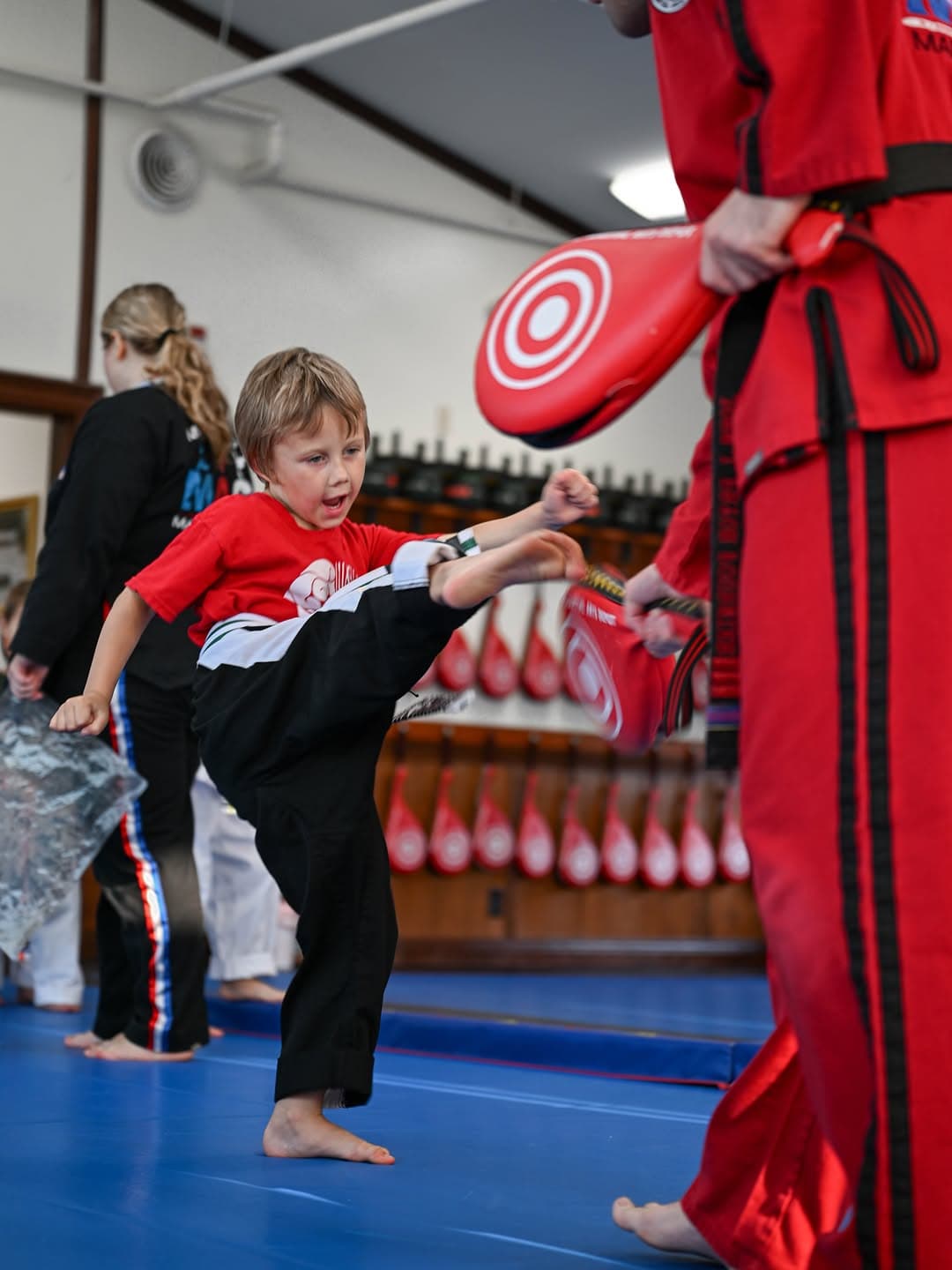 Small boy in a red dobok kicking a paddle on the blue mat