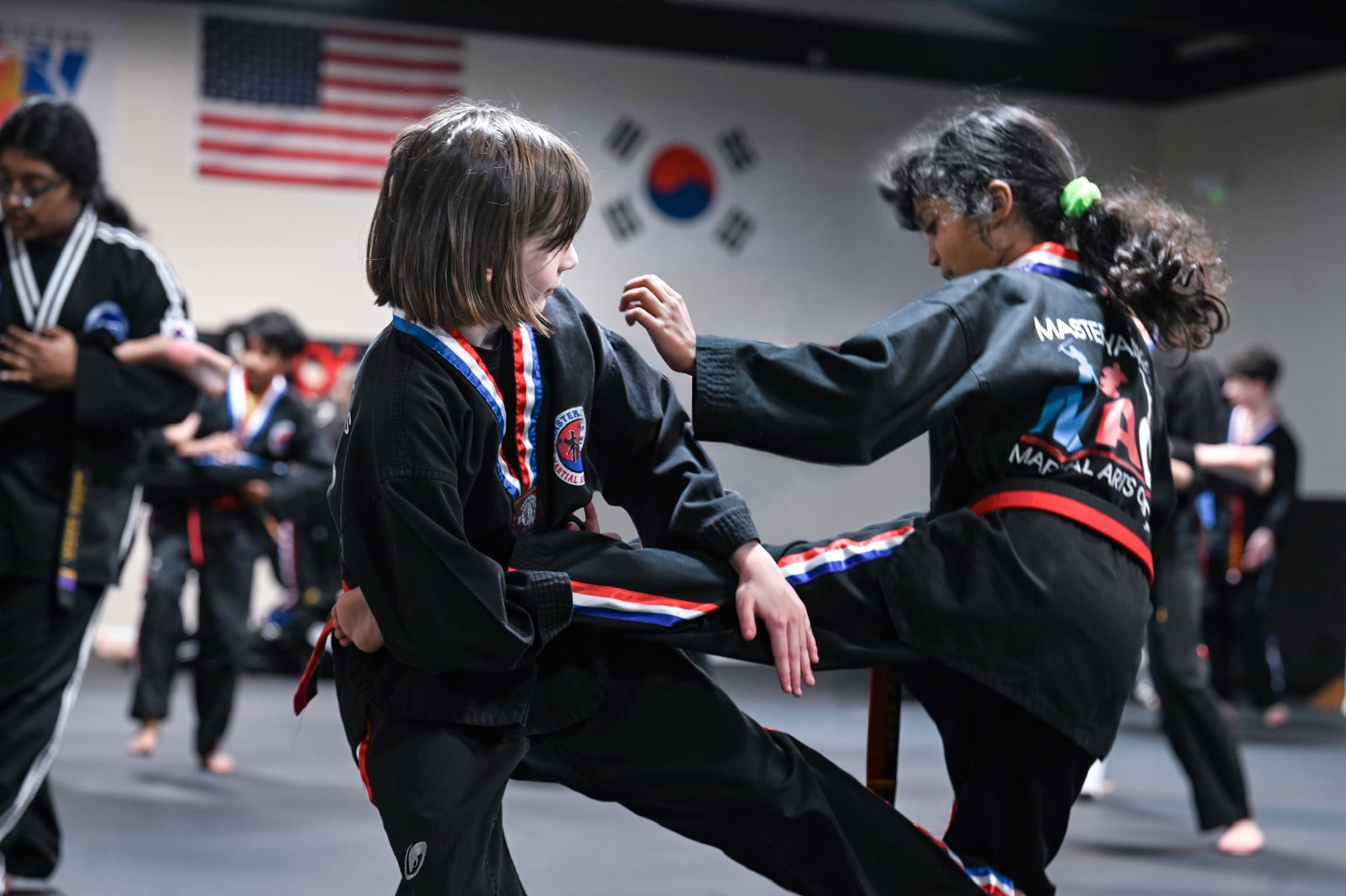 Girl in a black dobok kicking a pad held by an instructor