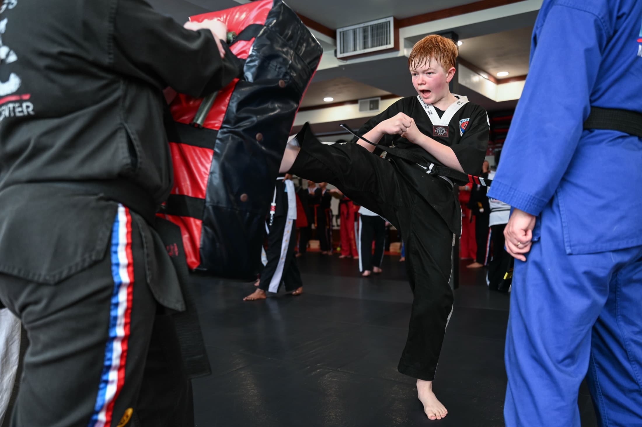 Boy in a black dobok driving a front kick into a pad