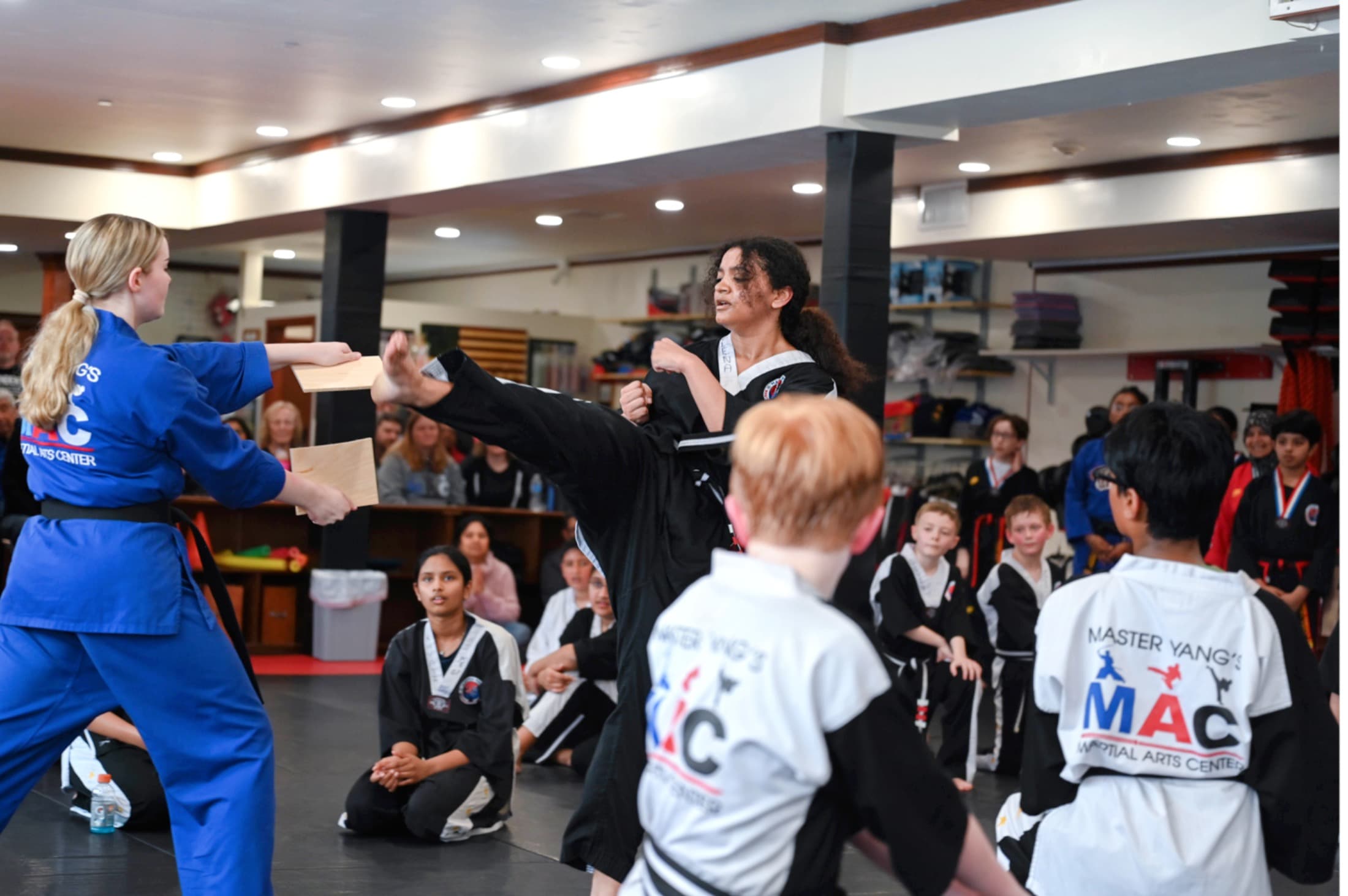 Instructor holding a board for a child to break while other children watch
