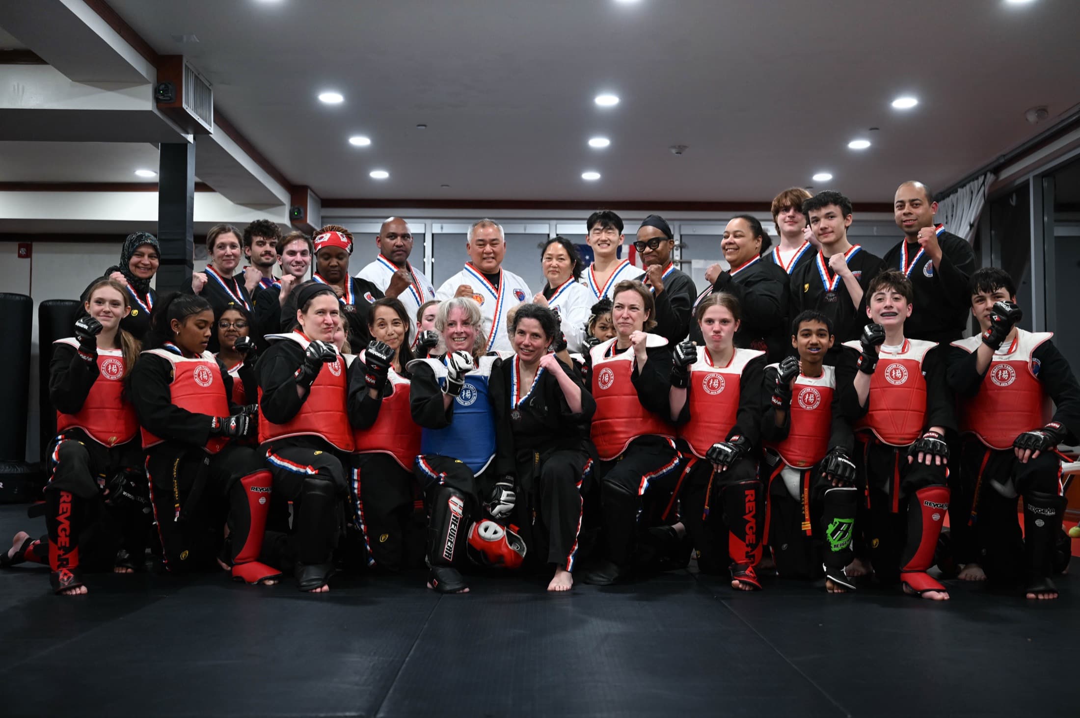 A large group of students and adults in red sparring gear, Grandmaster Yang among them