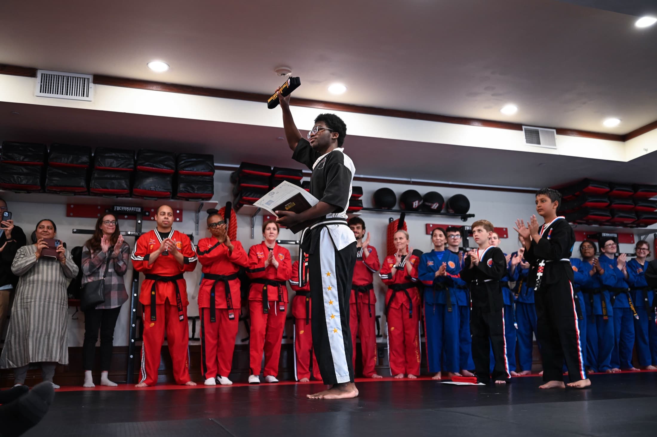 Instructor holding a board aloft in front of a line of students, parents watching