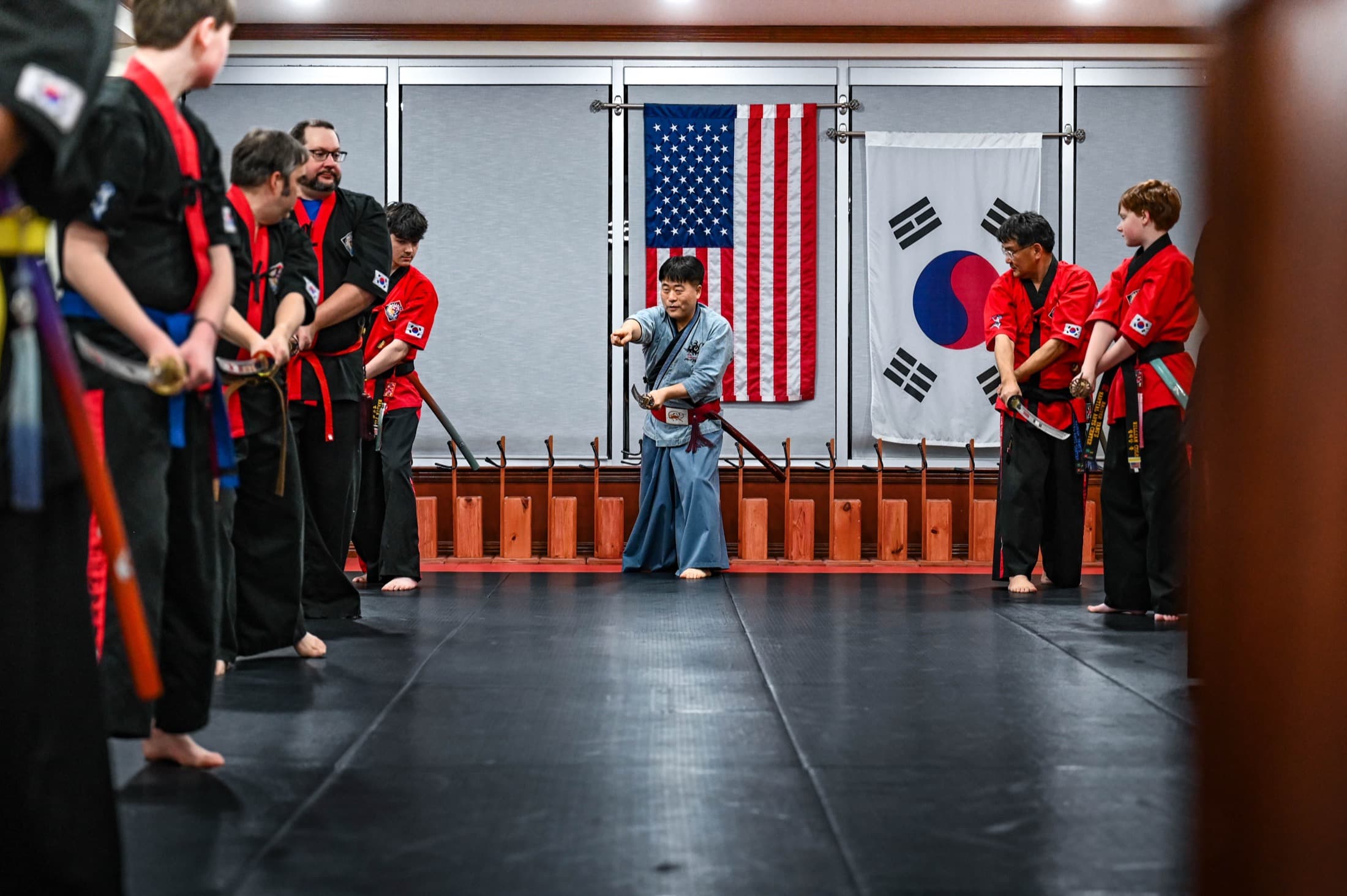 A line of students holding practice swords with their instructor under the US and Korean flags