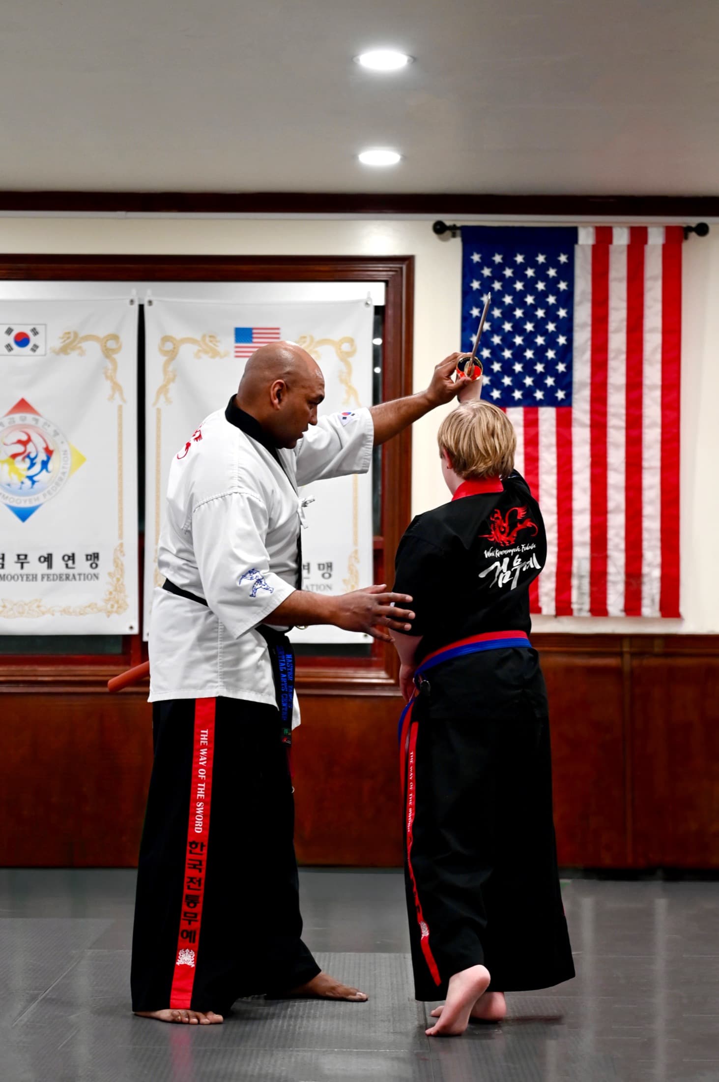 Instructor tying a young student's belt in front of the flags